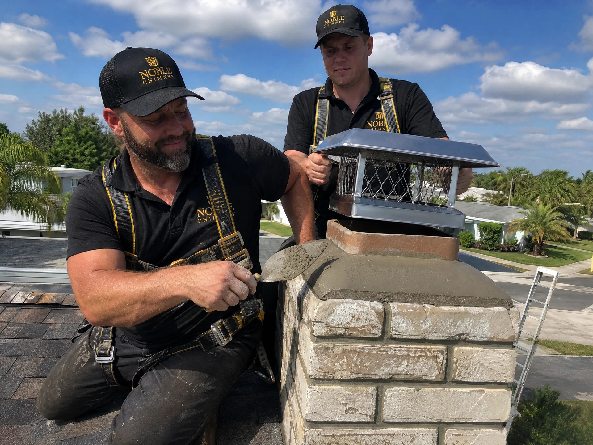 Noble Chimney masons repairing a chimney crown and installing a stainless cap on a rooftop