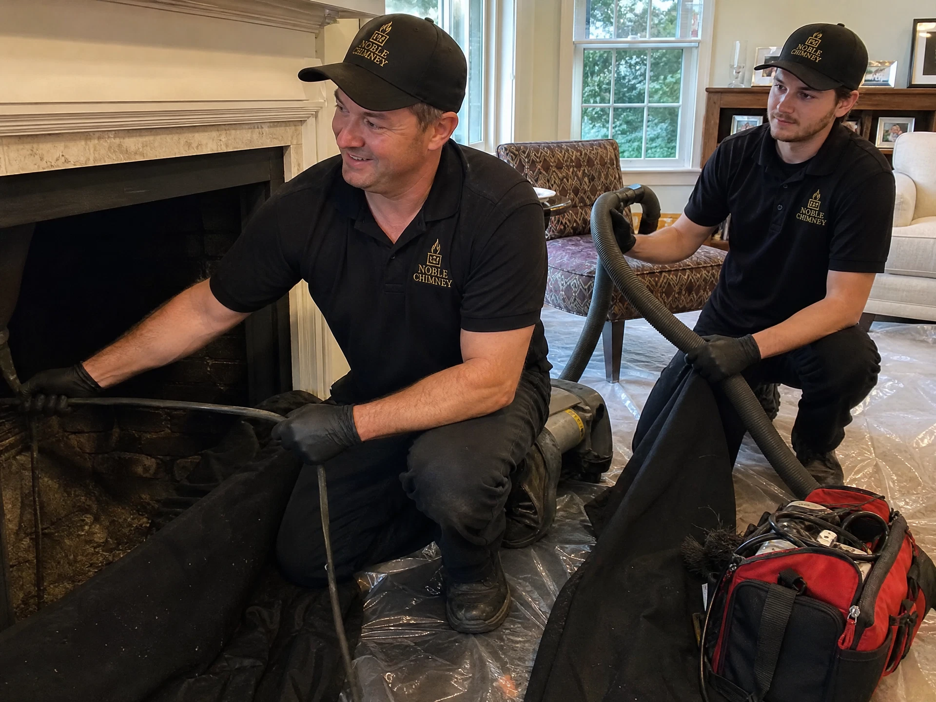 Two Noble Chimney technicians in branded shirts cleaning a fireplace flue together